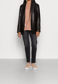 Blazer in pelle nera, felpa rosa chiaro, jeans scuri e sneakers beige senza lacci. Texture liscia, design aderente e dettagli di cucitura visibili.