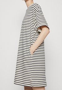 Gestreiftes T-Shirt-Kleid in Creme und Marineblau, mit lockerer Passform, kurzen Ärmeln, seitlichen Taschen und einem leichten Schlitz am Saum.