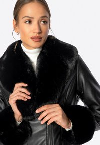 Černá kožená bunda s širokým, měkkým umělým kožíškem na límci a manžetách. Hladká textura s předním zapínáním na zip.