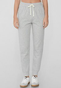 Grijze trainingsbroek met een comfortabele pasvorm, elastische tailleband, verstelbare trekkoord en geribde boorden. Gecombineerd met witte sneakers.