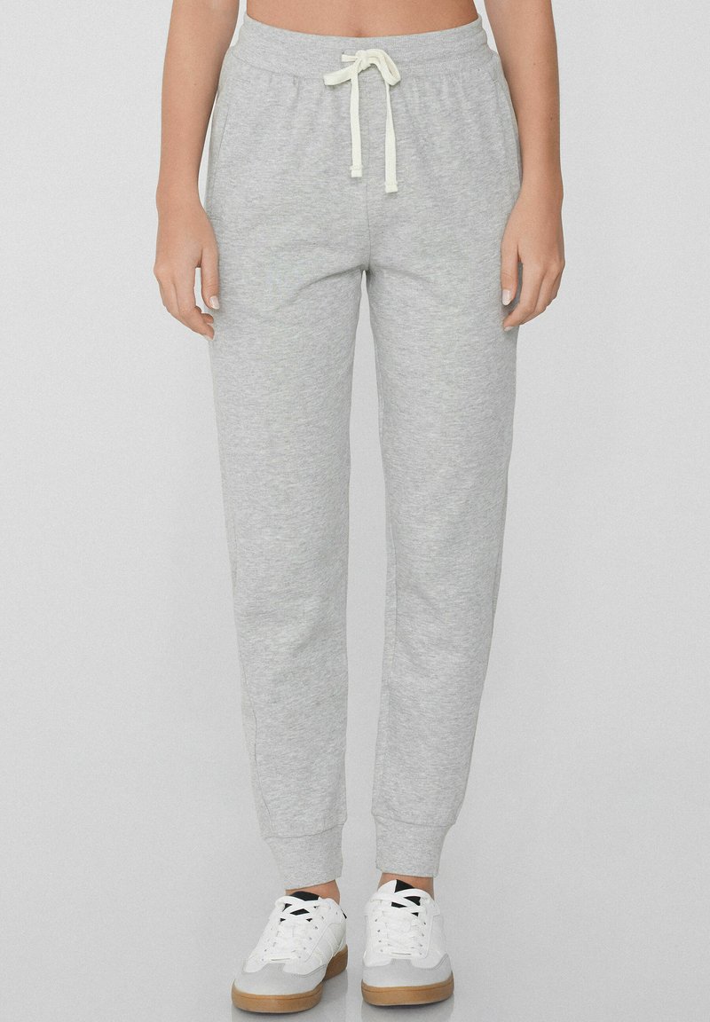 Grijze trainingsbroek met een comfortabele pasvorm, elastische tailleband, verstelbare trekkoord en geribde boorden. Gecombineerd met witte sneakers.