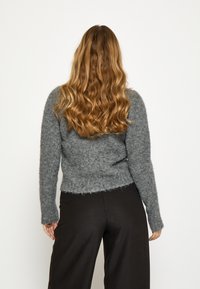 Sivý chlpatý sveter s priliehavým strihom, dlhými rukávmi a mierne skráteným okrajom. Nosený s čiernymi širokými nohavicami.