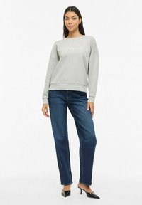 Grå genser med rund hals og lange ermer, kombinert med blå jeans med rette ben. Genseren har et dekorativt tekstmønster.