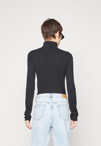 Maglietta nera a costine con maniche lunghe e colletto alto, abbinata a jeans alte in blu chiaro con una patta in pelle sul retro.