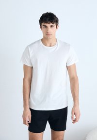 White cotton t-shirt with a crew neckline, short sleeves, and relaxed fit, paired with black shorts. Simple and minimalistic design.