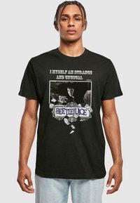 Sort bomulds T-shirt med et grafisk print med teksten "JEG SELV ER STRANDE OG UALMINDELIG" samt et billede af en karakter, udsmykket med et slangedesign.