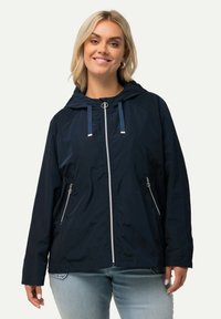 Marinblå vindjacka med huva, framdragkedja och silverdetaljer. Har justerbara huvningsband och två sidofickor med dragkedja.