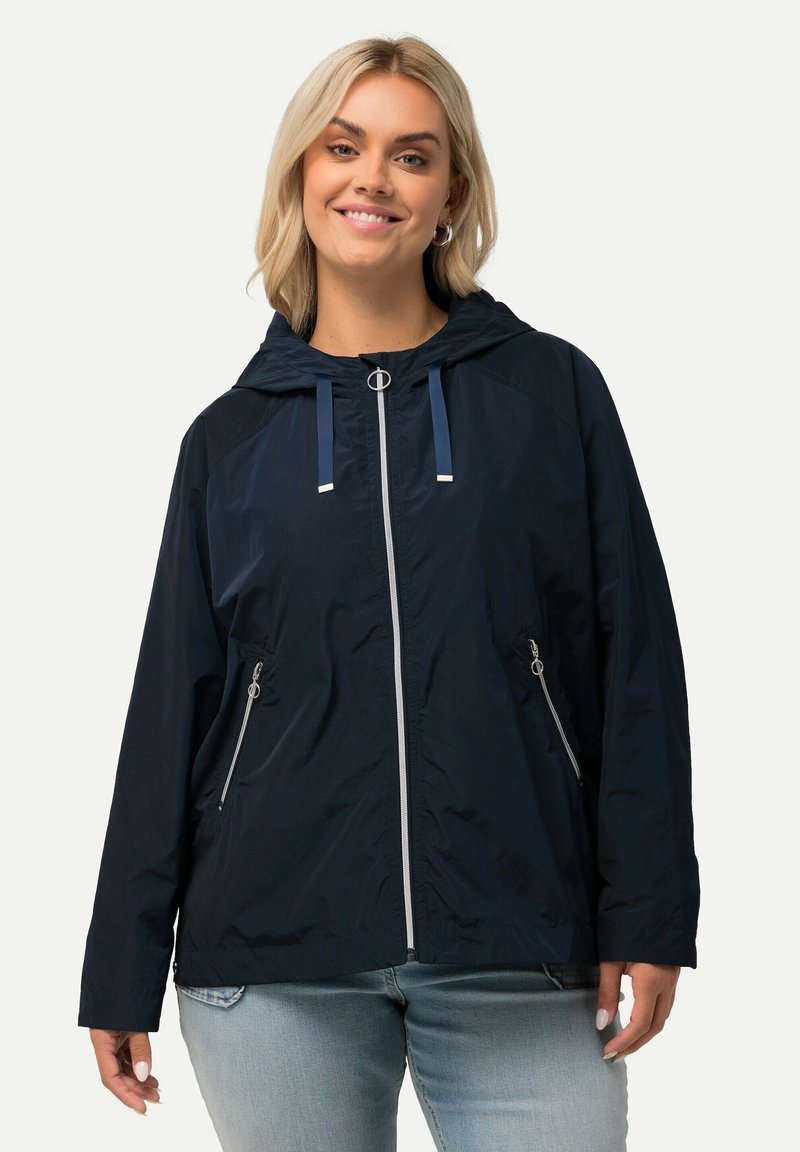 Marinblå vindjacka med huva, framdragkedja och silverdetaljer. Har justerbara huvningsband och två sidofickor med dragkedja.