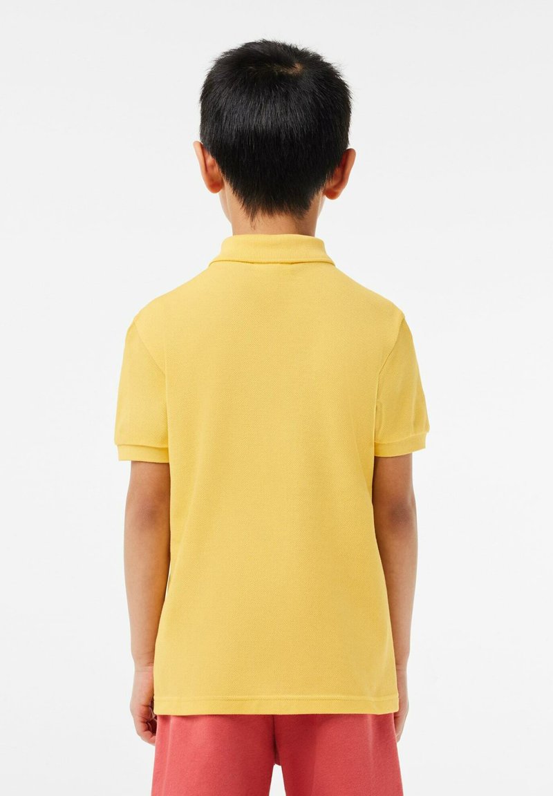 Polo shirt jaune vif avec un col côtelé et des manches courtes, fabriqué dans un tissu texturé. Porté avec un short rose.