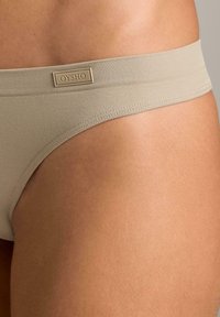 Intimo beige con una fascia testurizzata e una piccola etichetta OYSHO. Il tessuto appare liscio e presenta un taglio a vita bassa lungo la gamba.