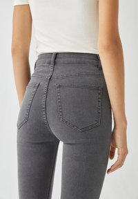 Jean gris taille haute en denim. Les caractéristiques incluent des poches arrière, une silhouette ajustée et une texture lisse.