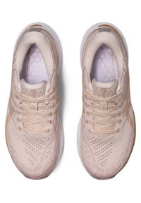 Baskets de sport rose clair avec un dessus en mesh texturé, bout arrondi, design à lacets, et semelle intermédiaire blanche. Semelle intérieure avec motif en nid d'abeille visible.