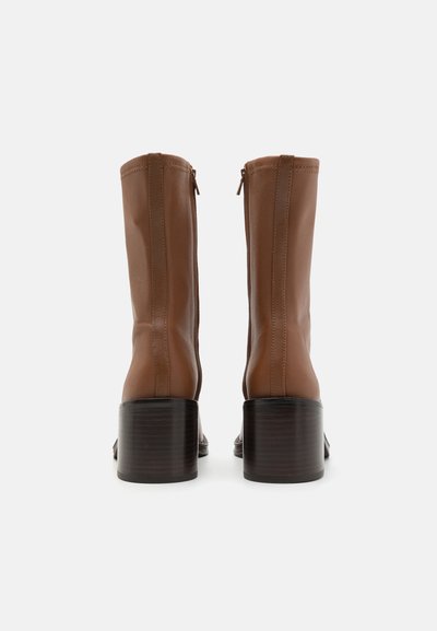 Bottines en cuir marron avec un design épuré, dotées d'une fermeture éclair latérale et d'un talon en bois empilé. Texture lisse, forme ajustée.