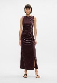 Μακρύ, αμάνι�κο φόρεμα από βελούδο σε σκούρο μπορντό, με ραφές στην μία πλευρά και σκισίματα μέχρι το μηρό για επιπλέον κομψότητα.