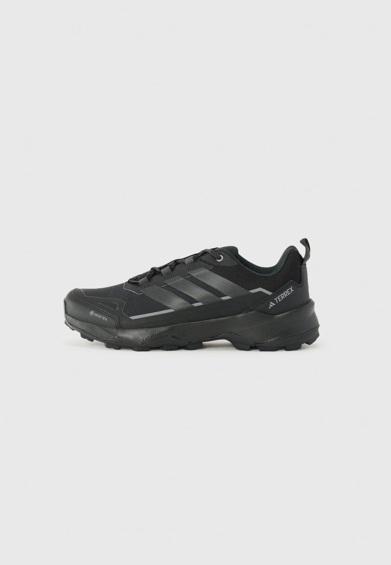 Black athletic shoe with a textured fabric upper, three silver stripes, reinforced toe, and a rugged rubber sole for traction.