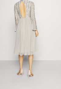 Une robe en tulle grise avec un décolleté dans le dos, des manches longues en sequins et une jupe évasée. Portée avec des sandales à talons hauts rose pâle.