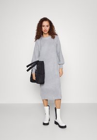 Harmaa ribbed midi-mekko puffattujen hihojen kanssa, yhdistettynä mustaan päällystettyyn laukkuun ja valkoisiin nilkkureihin, joissa on mustat pohjat. Sileä, tekstuuri kangas.