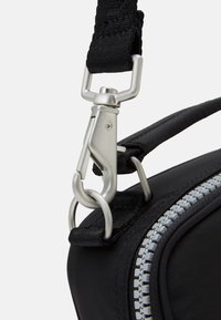 Pronto primo piano di una borsa di tessuto nera con una clip metallica argento, tracolla nera e dettagli della cerniera grigi. Texture liscia, design funzionale e resistente.