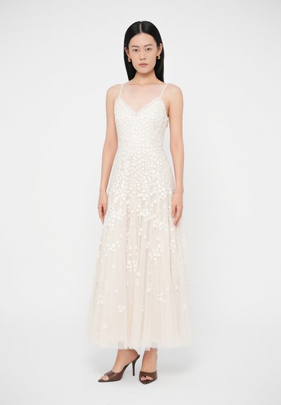 Μακρύ, ανοιχτό μπεζ φόρεμα με κεντήματα λουλουδιών, λεπτές τιράντες και εφαρμοστό μπούστο, που ρέει σε έναν πολύστιχο, διάφανο τούλινο φουστανέλα. Καφέ παπούτσια με τακούνι.