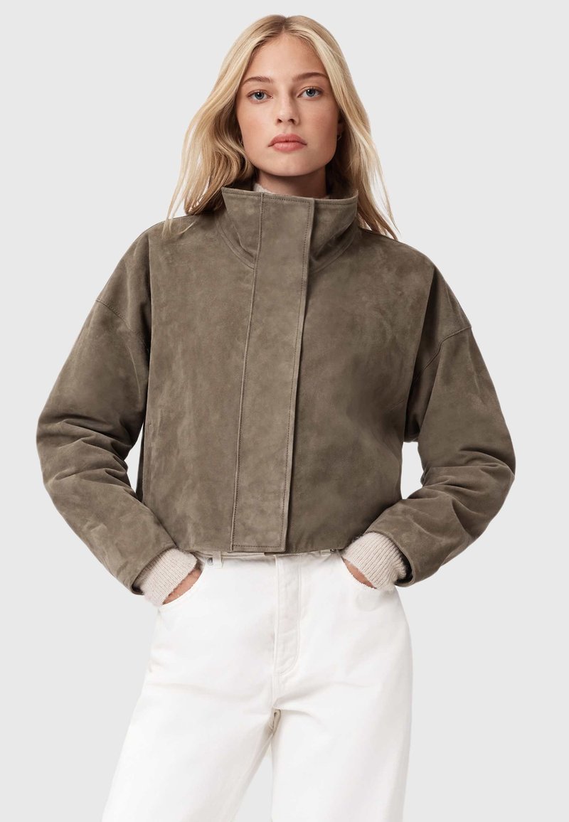 Zkrácená olivově zelená semišová bunda s vysokým límcem a volným střihem. Obsahuje ribbované pletené manžety a bezšvové zapínání vpředu.