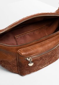 Borsa a tracolla in pelle marrone con tasca frontale con cerniera, ricamo floreale e scomparto principale aperto che mostra una tasca interna a toppa.