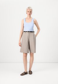 Gai zils bezpiedurkņu topiņš, bēša pielāgotas culottes ar krokām, melns jostas, un dzīvnieku printa čības. Tīrs dizains uz neitrāla fona.