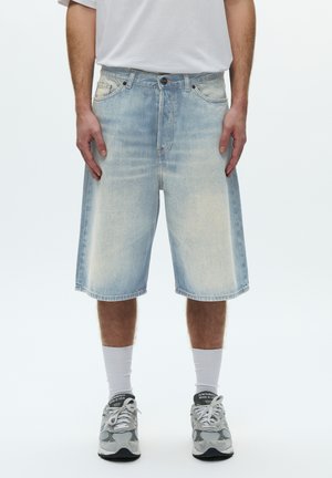 Shorts di jeans azzurri chiari con una vestibilità ampia, che arrivano a metà polpaccio. Presentano un design classico a cinque tasche e orlo grezzo. Abbinati a sneaker grigie.