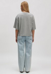 Graues T-Shirt mit kurzen Ärmeln und entspannter Passform, kombiniert mit hellblauen, weit geschnittenen Jeans, die ein klassisches Fünf-Taschen-Design aufweisen.