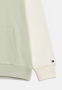 Sudadera verde y blanca con un bolsillo frontal, dobladillo acanalado y manguitos. Detalle de logo notable en rojo, blanco y azul en el puño.