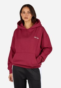 Bordový mikina s veľkou prednou vreckom, kapucňou so šnúrkou, voľným strihom a vyšitým logom "COZY CLUB" na hrudi. Mäkka bavlnená tkanina.