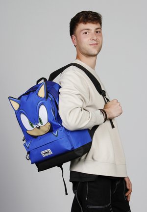 Mochila de tela azul con un gráfico de Sonic the Hedgehog, correas ajustables negras, un asa superior y una base negra para mayor estabilidad.