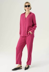Completo due pezzi magenta composto da una camicia con bottoni a maniche lunghe e pantaloni dalla vestibilità rilassata. Indossato con ballerine nere a punta e occhiali da sole.