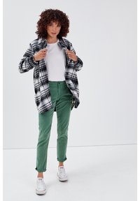 Zwart-witte geruite fleece jas, witte t-shirt, groene broek en witte sneakers. De jas heeft een relaxte pasvorm en een zachte textuur.