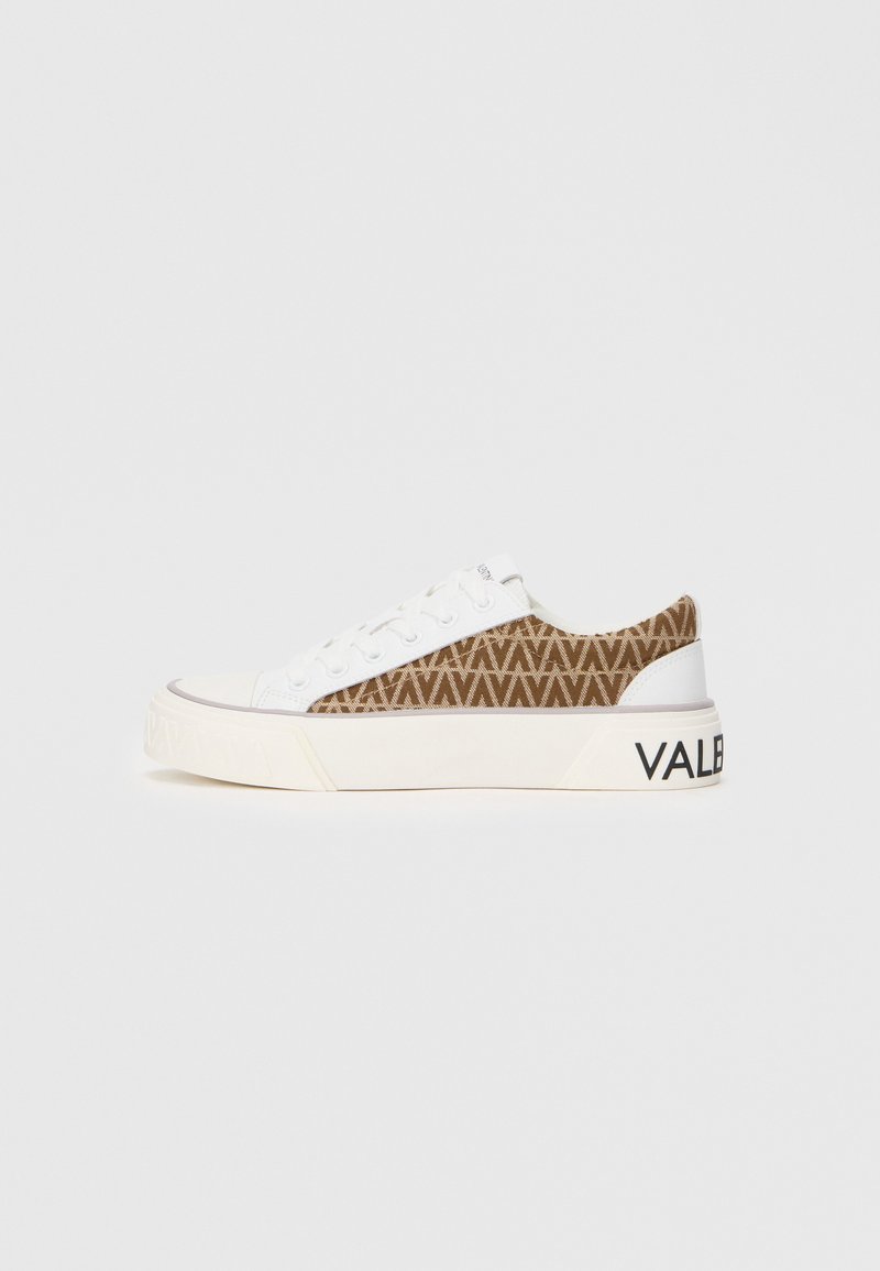 Bijela tenisica s smešnim geometrijskim uzorkom sa strane, koja ima ravnu obuću i "VALENTINO" oznaku na peti.