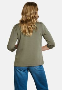 Chemise à manches longues vert olive avec un ourlet arrondi et des coutures simples. Associée à un jean bleu, vue de dos.