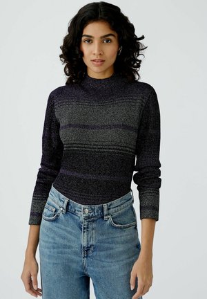 Gestrickter Langarm-Top in Dunkelpurple mit helleren horizontalen Streifen. Hoher Kragen und enganliegendes Design, kombiniert mit hellblauen High-Waist-Jeans.