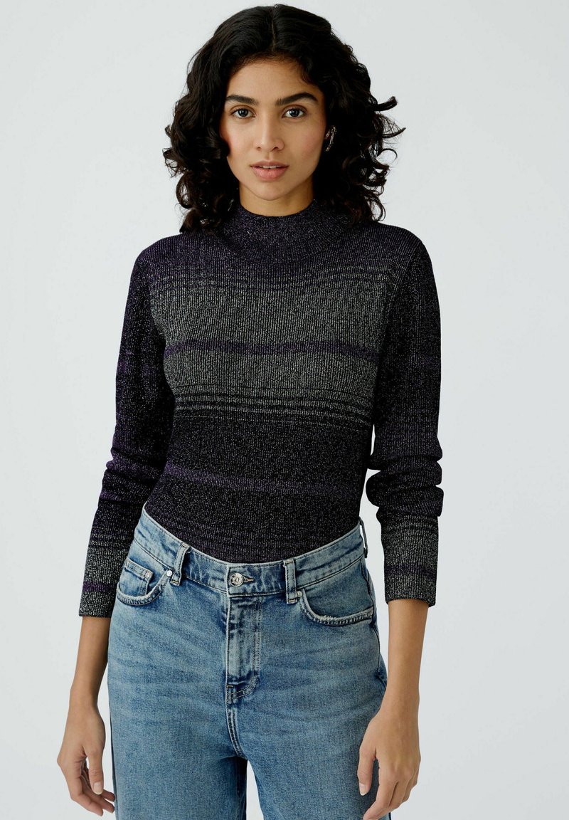 Gestrickter Langarm-Top in Dunkelpurple mit helleren horizontalen Streifen. Hoher Kragen und enganliegendes Design, kombiniert mit hellblauen High-Waist-Jeans.