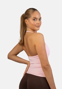 Jasnoróżowy top na ramiączkach o dopasowanym kroju, z cienkimi ramiączkami i marszczeniem na plecach, zestawiony z ciemnobrązowymi legginsami.