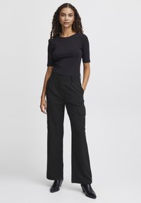 Zwart aangesloten t-shirt gecombineerd met hoog-waist zwarte broek met cargozakken, wijde pijpen en een subtiele textuur in de stof.