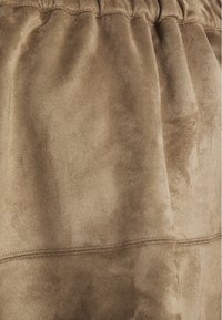 Tissu suédine taupe avec une surface douce et texturée et une taille froncée. Présente des détails de couture subtils pour plus de structure.