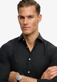 Camicia nera con bottone e una leggerissima texture, dotata di colletto a sacchetto e bottoni bianchi. Autenticata da un logo ricamato sul petto.