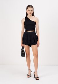 Svart en-skulder crop top, lagde svarte volangshorts, svart håndveske, og stroppede høyhælte sandaler med dekorative accenter.