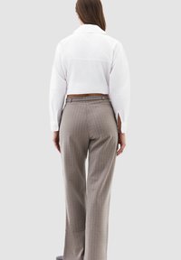 Camicetta bianca a maniche lunghe e taglio corto, abbinata a pantaloni beige a righe sottili a vita alta. Vestibilità sartoriale e texture del tessuto liscia.