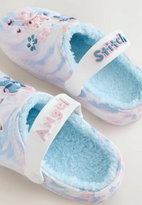 Zuecos coloridos con un patrón de mármol rosa y azul, forrados con suave piel de oveja azul, y adornos de personajes moldurados, con correas blancas etiquetadas como "Ángel" y "Stitch".