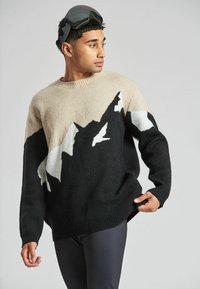 Schwarzer, beige und weiß gemusterter Strickpullover mit Bergmotiven; gerippter Halsausschnitt und Saum; Modell trägt Skibrille.