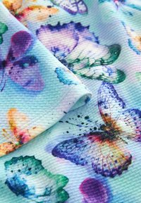 Textile présentant un fond turquoise avec des imprimés de papillons multicolores, affichant des nuances variées de violet, bleu et vert.