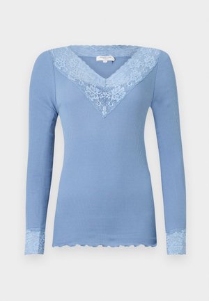 Blå långärmad topp med ribbad textur, scalloped spetsdetaljer vid halsringning och ärmar, med blommig spetsdekoration i ljusblått.