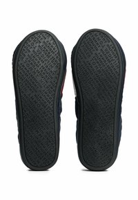 Suole delle scarpe con superficie in gomma testurizzata, caratterizzate da una base grigia scura e lettere in rilievo orientate in varie direzioni, offrendo trazione e durabilità.