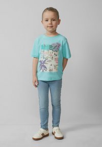 Turquoise t-shirt met een strandthema graphic, gecombineerd met lichtblauwe jeans en witte sneakers met bruine accenten. Gladde stoftextuur.