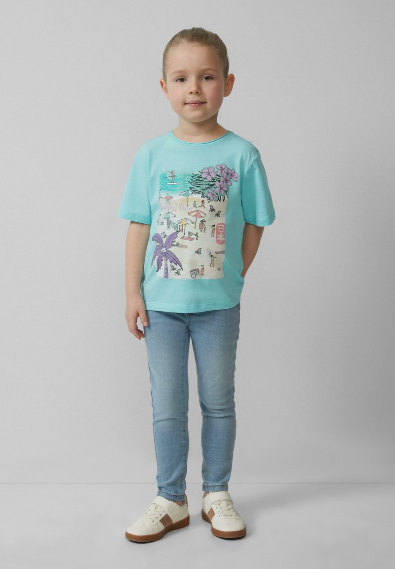 Turquoise t-shirt met een strandthema graphic, gecombineerd met lichtblauwe jeans en witte sneakers met bruine accenten. Gladde stoftextuur.